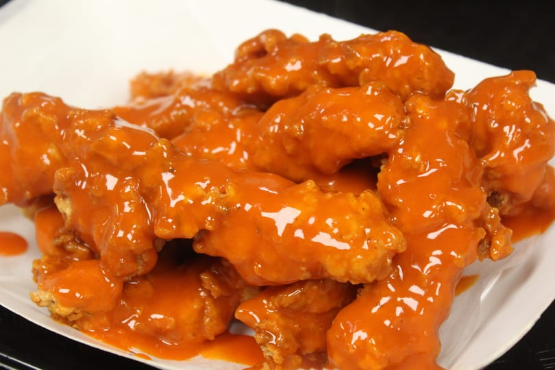 Pile of boneless chicken wings covered in shiny orange buffalo sauce on a white plate.