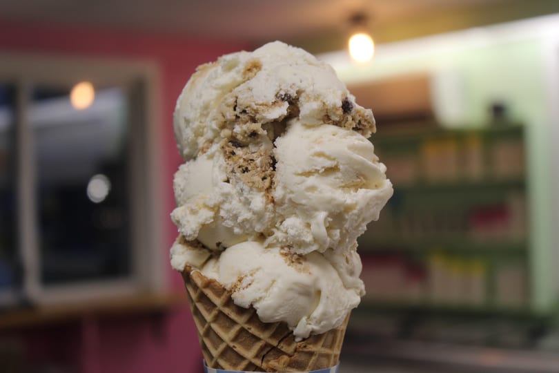 Multiple scoops of white ice cream with cookie chunks in a waffle cone.