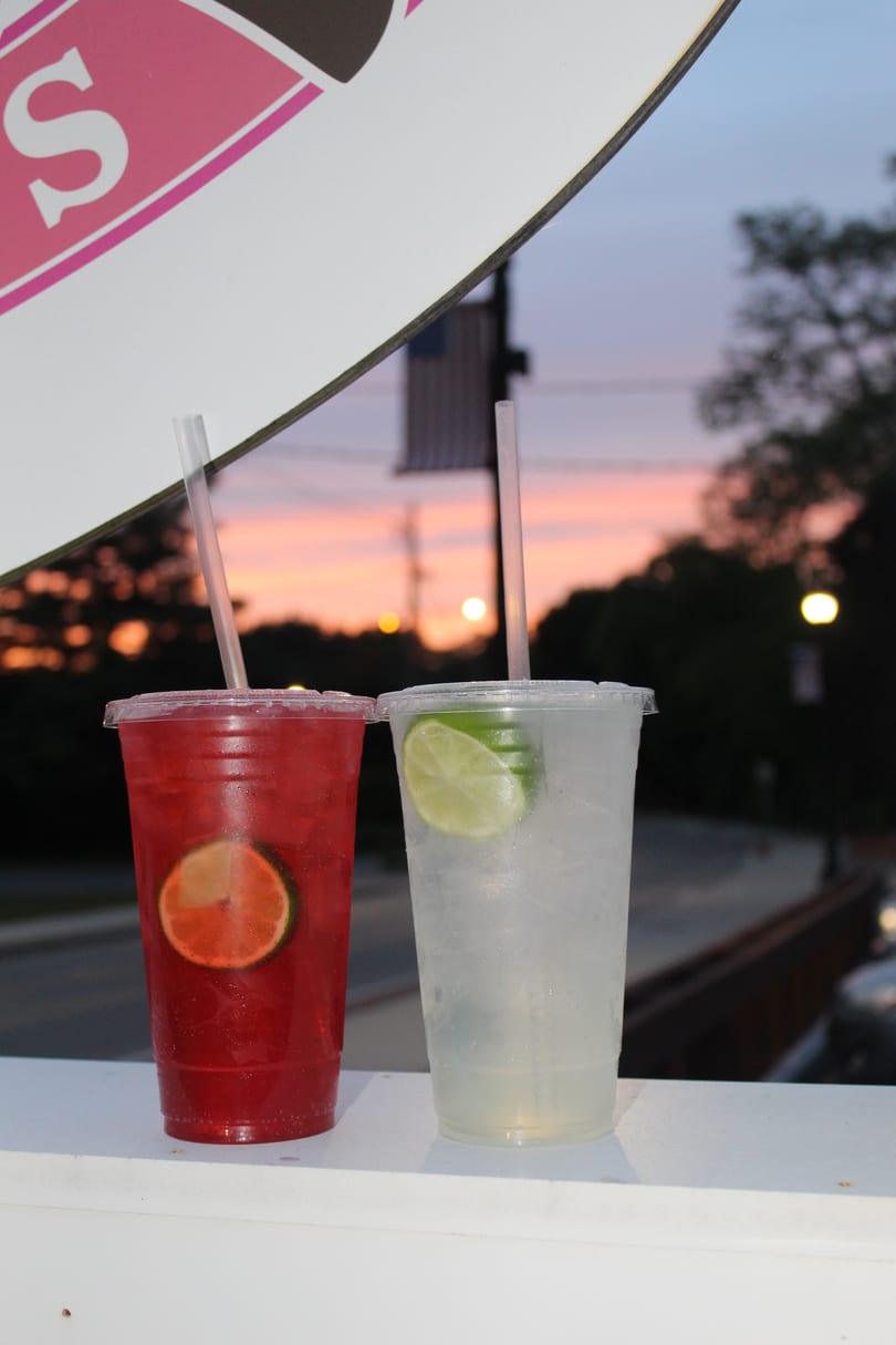 Two iced drinks, red and clear with lime, on a white surface at sunset.
