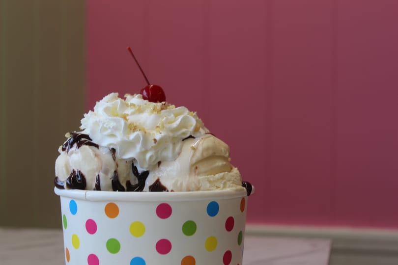 Ice cream sundae with chocolate, whipped cream, nuts, and a cherry in a polka dot cup.